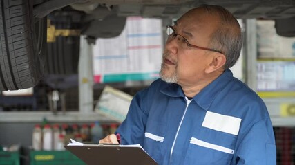 asian mechanic senior man holding clip board checking list to brake ,tyre, undercarriage of a car in workshop at auto car repair service center. car engineer old man inspection vehicle details