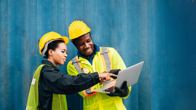 worker team man and woman in protective safety jumpsuit uniform with yellow hardhat and use laptop check container at cargo shipping warehouse. transportation import,export logistic industrial service