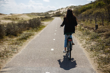 Fototapeta premium Full length image. Back view of a young girl walks single on bicycle on the road in sunny day time.