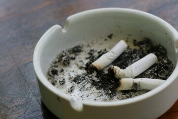 Cigarettes in ashtray at smoking area. Cigarettes and tobacco lying inside ceramic ash tray on the outdoor table. World no tobacco day on may 31. Selective focus.