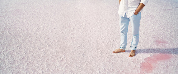 Panoramic image man legs barefoot standing on salt flats on pink salt lake, crystallized salt...