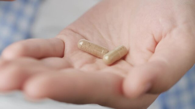 Two big transparent cylindrical pill capsules with green powder inside fall into palm of hand from pill bottle. Close-up, front view, center composition
