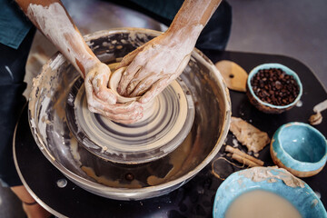 Close-up of the hands of a woman ceramist working with a potter's wheel in a cozy, bright workshop. A young experienced woman skillfully makes a mug, vase or plate. Creative people, pottery workshop
