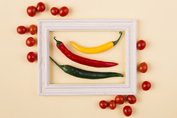 Minimal concept of red, yellow and green pepperoni in the middle of wooden frame with tomatoe outside against pastel background.  Creative layout