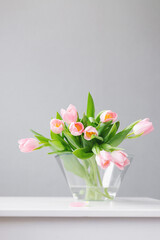 pink tulips in a large glass vase stand on the table, on a gray background, space for text, free space, floristry, florist, tulip bouquets, bouquet, valentine's day, international women's day,flowers