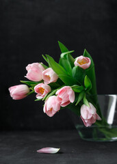pink tulips with green leaves in a glass vase, on a black background, florist, floristry, gift, bouquet, bouquet for a girl, a bouquet of tulips, place for text, place for an inscription, beautiful