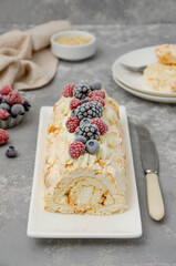 Meringue roll Pavlova cake with cream and raspberries, blackberries and blueberries on top on a gray background. Copy space.