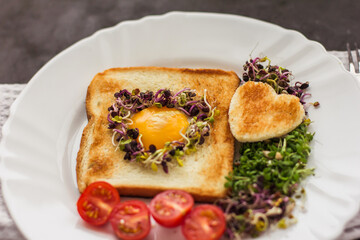 Egg in a hole of bread heart shape, microgreens, healthy food Breakfast, tea, black background