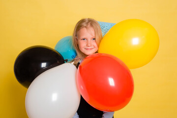 Fototapeta na wymiar A girl in a school uniform with a festive cap on her head is holding balloons in her hands isolated on a yellow background.