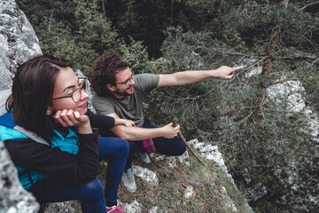 Couple taking a break while hiking, sitting at a viewpoint, pointing and looking at distance