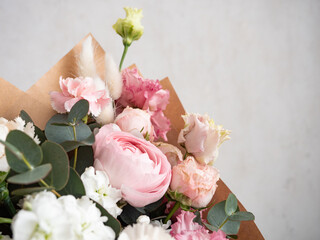 Delicate bouquet of dianthus, rose, ranunculus and eucalyptus in craft paper in the morning light