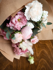Delicate bouquet of dianthus, rose, ranunculus and eucalyptus in craft paper in the morning light
