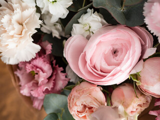 Delicate bouquet of dianthus, rose, ranunculus and eucalyptus in craft paper in the morning light