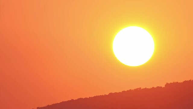 Time-lapse of sunrise with orange sky background, sun rising from mountaintop