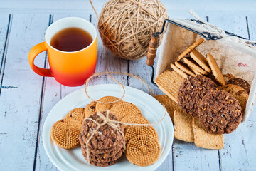 Assorted biscuits in plate and basket and a cup on blue table