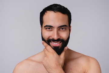 Smiling good-looking moroccan man touching his beard before shaving isolated over grey background