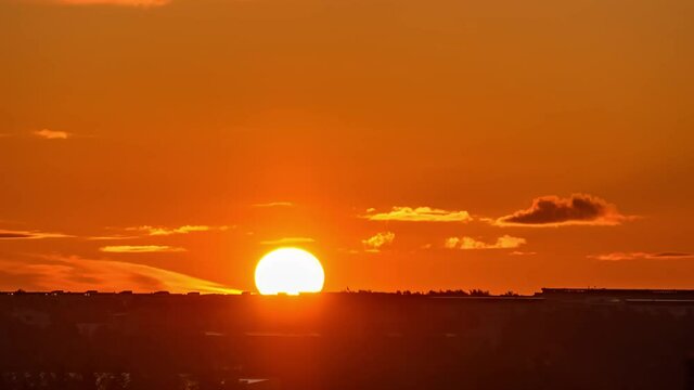 Time-lapse of sunrise and silhouettes of city, rising sun and floating clouds in orange sky