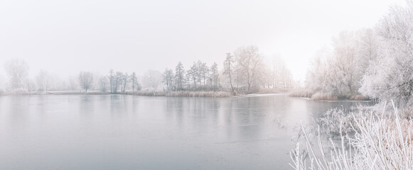 Obraz na płótnie Canvas Frozen lake in snowy forest landscape. White sky soft sunset sunrise light, idyllic white nature. Winter scow scenery, seasonal nature