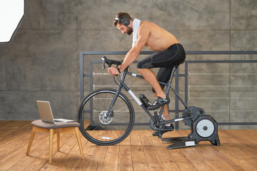 Handsome young man listening to music and riding stationery bike