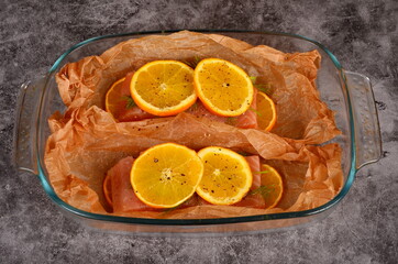 Orange slices placed on two fresh salmon fillets. Fish on baking paper, gray background