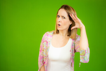 Young woman over isolated green background listening to something by putting hand on the ear