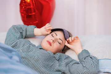 A healthy young woman in pajamas wakes up from sleep, removes her sleep mask