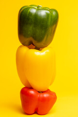 Green, yellow and red colorful peppers stacked on top of each other balancing. Studio food still life contrasted against a seamless dark yellow background.