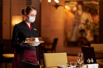 Responsible woman in mask tables and serving food