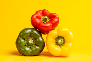 Grouping of red, yellow and green colorful peppers or paprika stacked on top of each other. Studio food still life contrasted against a seamless dark yellow background.