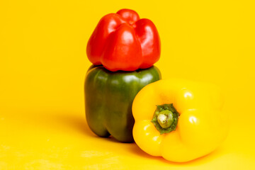 Couple of yellow, red and green colorful peppers stacked on top of each other. Studio food still life contrasted against a seamless dark yellow background.