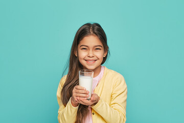 Portrait mixed race female kid with a glass of milk in her hands, isolated on turquoise background. Milk is good for children's health