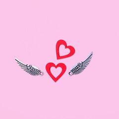 Two red hearts with silver wings on a pink background