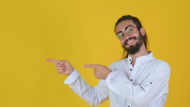 Happy young guy in glasses Look camera pointing fingers hands on copy space workspace isolated on yellow studio background. People lifestyle concept.