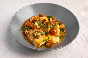 Traditional Sicilian fish with tomatoes, olives, parsley and red pepper in a deep plate on a light background, close up