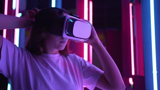 Beautiful young woman putting a VR headset against the background of multi-colored neon lamps