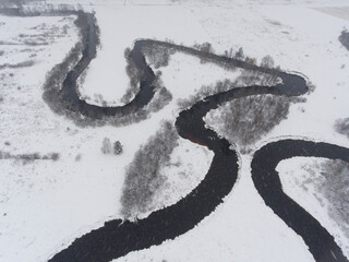 Beautiful winter nature. Aerial view of curved river. Snowy forest and field.