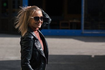 young beautiful smiling stylish blonde woman in sunglasses, black pants and leather jacket posing...