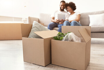 Moving Boxes Standing On Floor, Black Couple Using Tablet Indoor