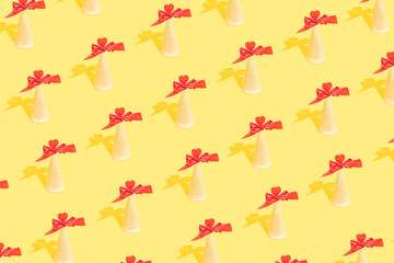 An ice cream cone with a red bow and heart symmetrically arranged in a pattern on a pastel yellow...