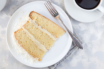 Piece of coconut cake with cream cheese frosting and coconut flakes decoration, on white plate, horizontal, top view