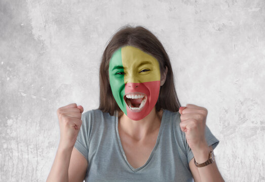 Young woman with painted flag of Benin and open mouth looking energetic with fists up