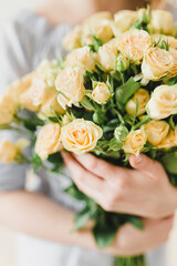 A bouquet of small beige roses in the hands of the girl. Light background, pastel shades, tenderness, spring.