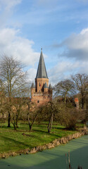 Fototapeta na wymiar Vertical panorama showing green winter barren gardens, blue sky with clouds and Drogenapstoren of medieval Hanseatic city Zutphen in The Netherlands in the background