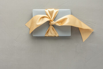 Gray gift box with golden bow on a gray concrete background, birthday or valentine concept, top...