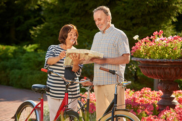Bike traveling mature couple looking at the map. Summer garden park background.