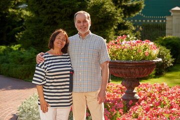 Portrait of happy mature couple in the garden. Smiling senior married couple. Flowers and trees background.