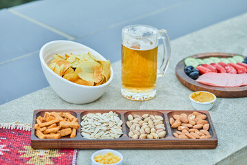 Assorted snacks, chips, a plate of sausages and a glass of beer on stone table