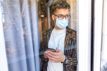 Man at the window in quarantine holding phone - obrazy, fototapety, plakaty