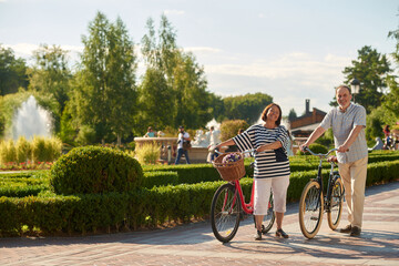 Fototapeta premium Senior man and woman with bikes outdoors. Sunny city park background.