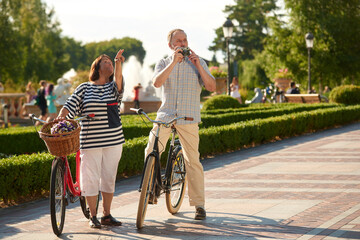 Happy retired loving couple with bikes and photo camera. Senior tourists with bikes outdoors.